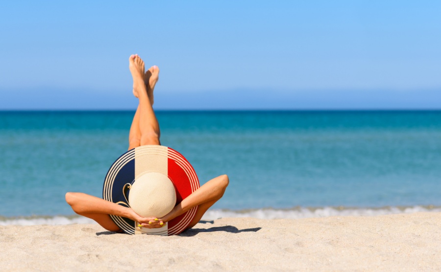 A slender tanned girl on the beach in a straw hat in the colors of the flag of France. The concept of a perfect vacation in a resort in France. Focus on the hat.