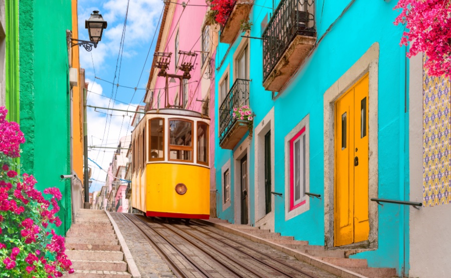 Lisbon, Portugal - Yellow tram on a street with colorful houses and flowers on the balconies - Bica Elevator going down the hill of Chiado